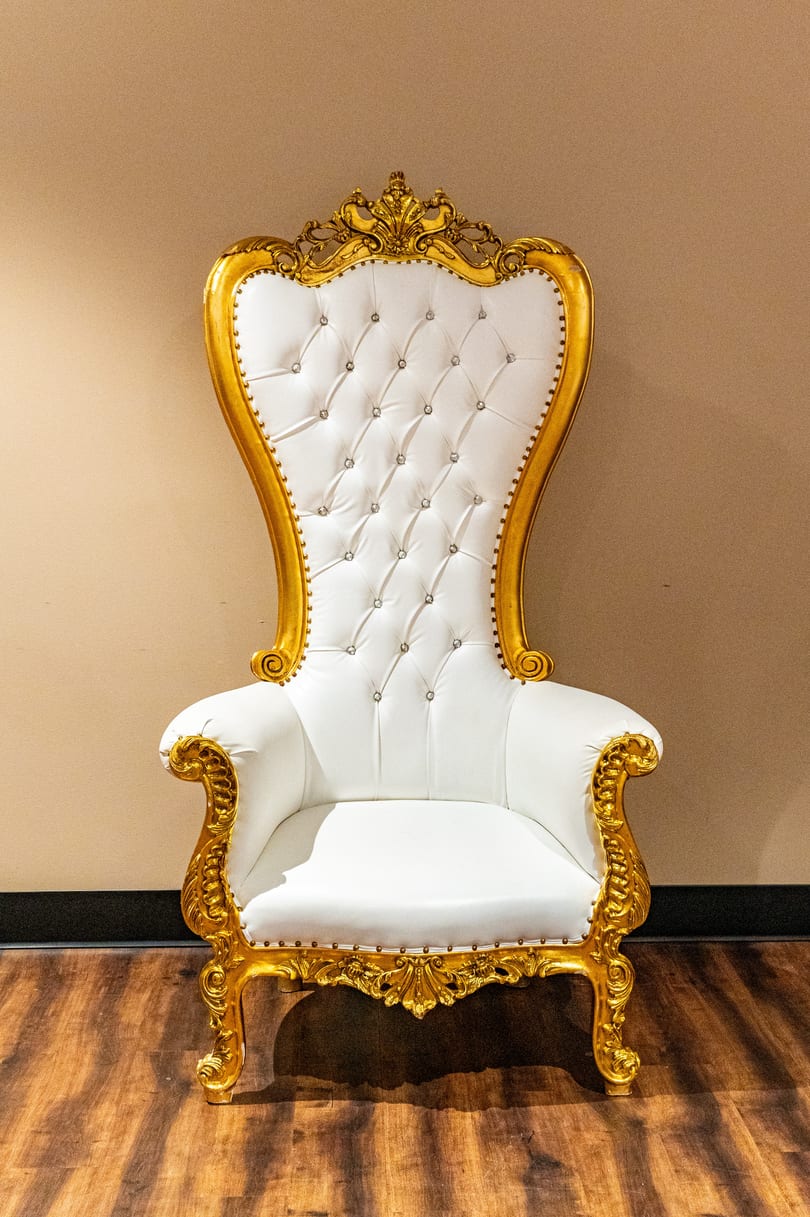 Ornate white and gold throne chair with tufted upholstery and sparkling accents on a wooden floor.