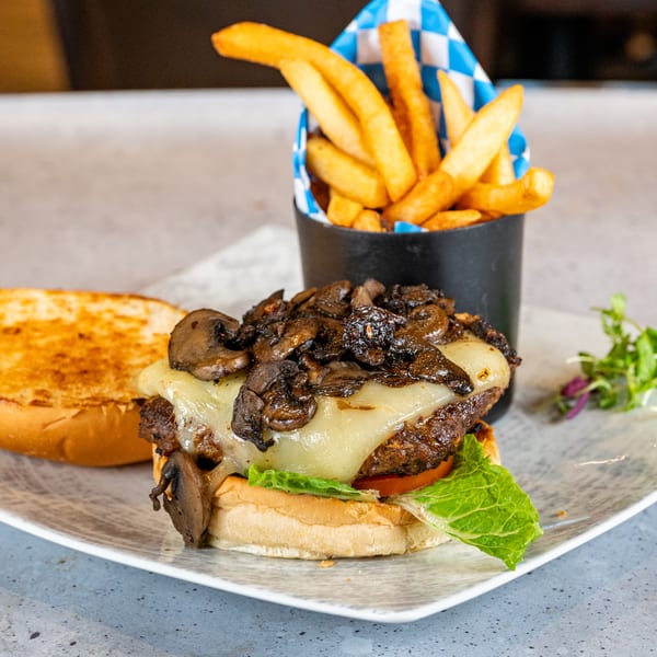 Mushroom Swiss burger with lettuce, tomato, and a side of fries in a blue and white checkered cup.