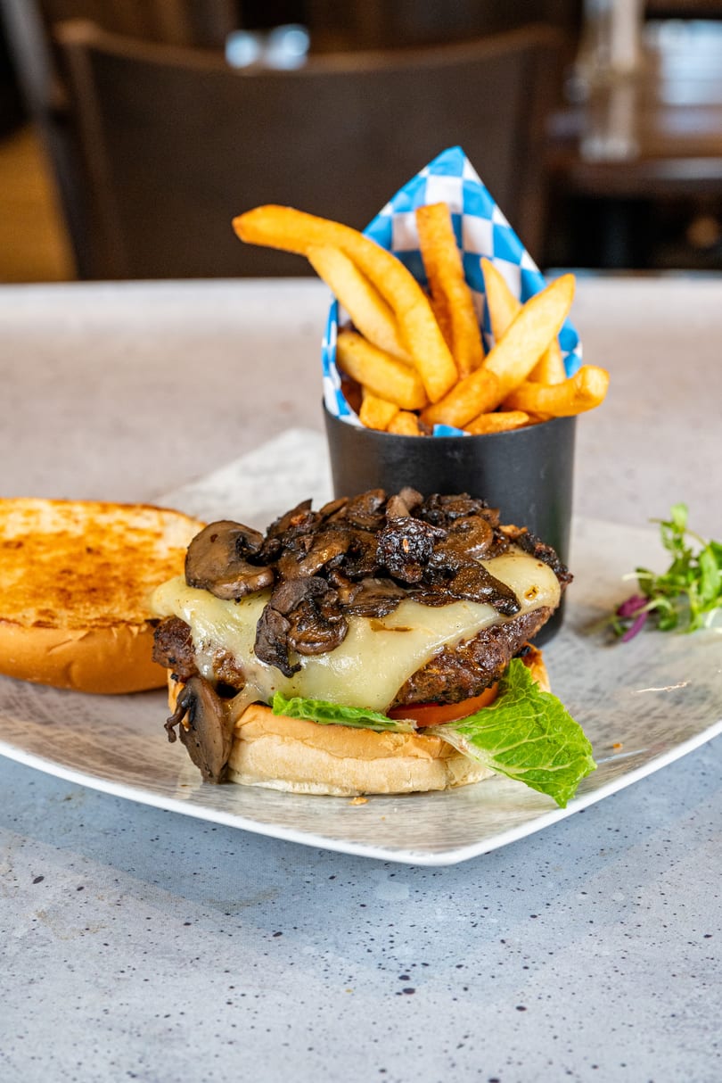 Mushroom Swiss burger with lettuce, tomato, and a side of fries in a blue and white checkered cup.