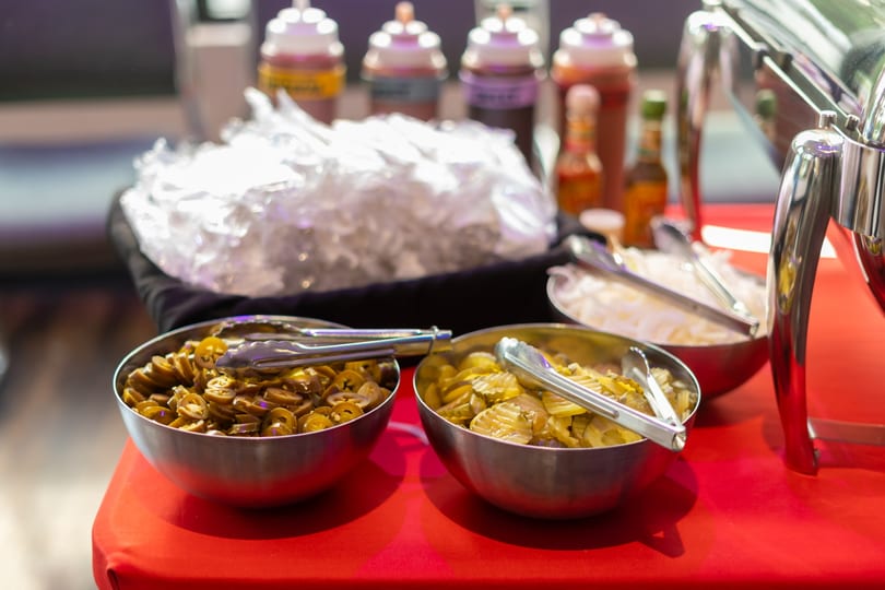 A buffet table with bowls of sliced jalapeños, pickles, onions, and various sauces.