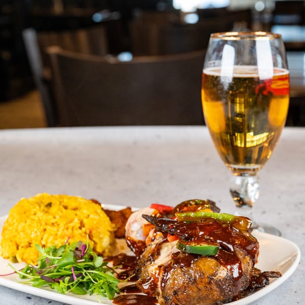 A plate of BBQ chicken, yellow rice, salad, and a glass of beer on a counter.
