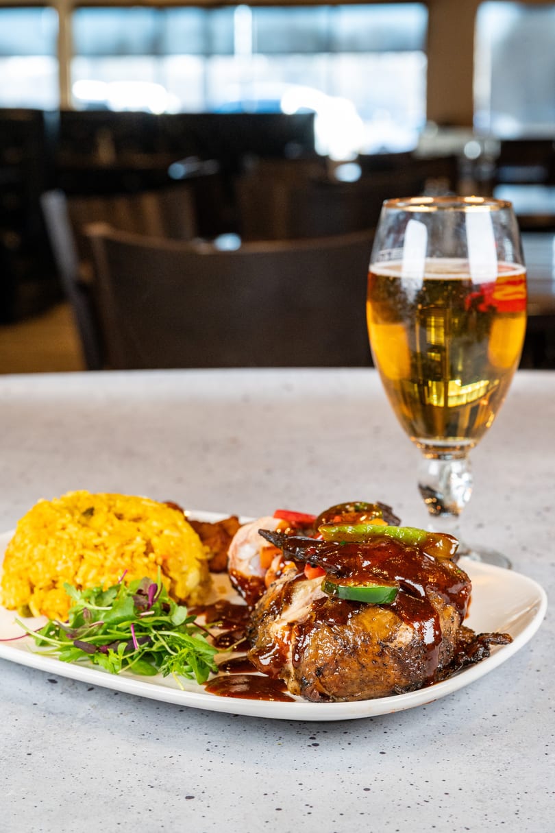 A plate of BBQ chicken, yellow rice, salad, and a glass of beer on a counter.