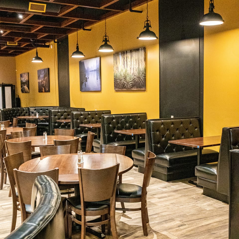 Restaurant dining room with yellow walls, black booths, wooden tables, and hanging industrial lights.