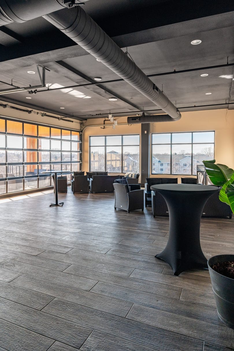 Spacious event room with large windows, modern seating, high-top tables, and exposed ceiling ducts.