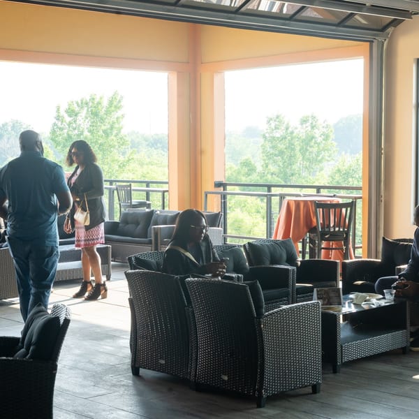 People relaxing in a spacious outdoor lounge area with wicker furniture and a scenic view.