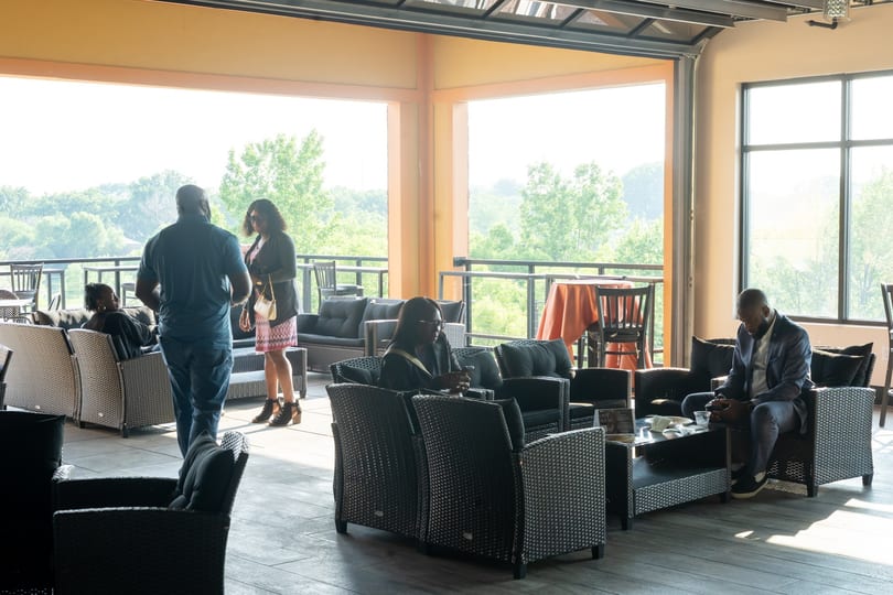 People relaxing in a spacious outdoor lounge area with wicker furniture and a scenic view.